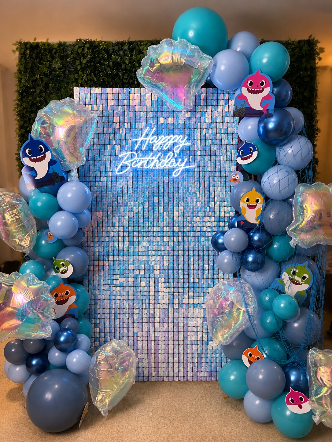 Blue shimmer wall example with blue balloon garland, Baby Shark accents, iridescent shell balloons, and Happy Birthday neon sign