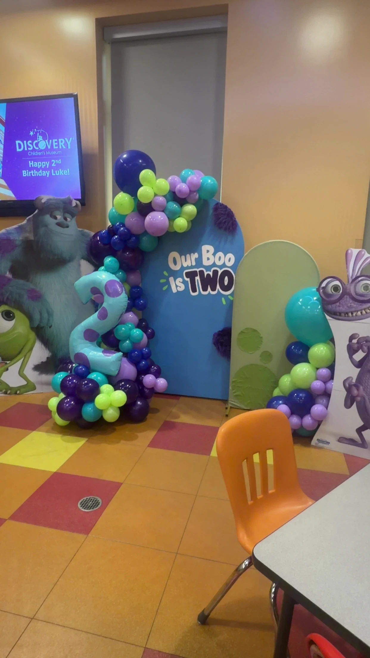 Monsters, Inc. second birthday setup with blue and green arch backdrops, turquoise, lime and purple balloons and character cutouts